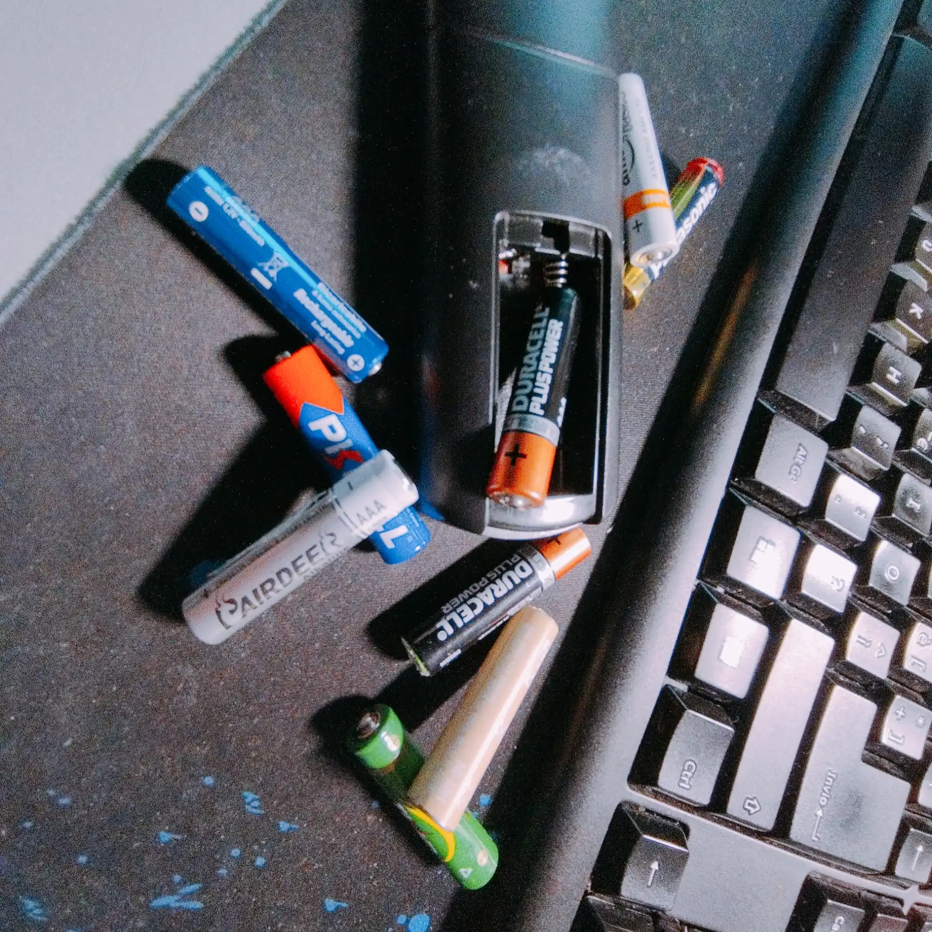 Il telecomando sulla mia scrivania, con il vano batterie aperto, e un sacco di batterie mini-stilo colorate attorno.